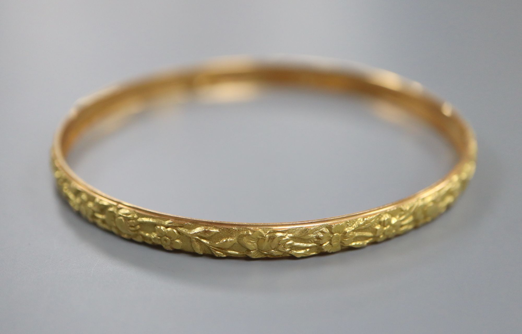 A yellow metal (tests as 18ct) bangle cast with continuous band of flowers, 9g,